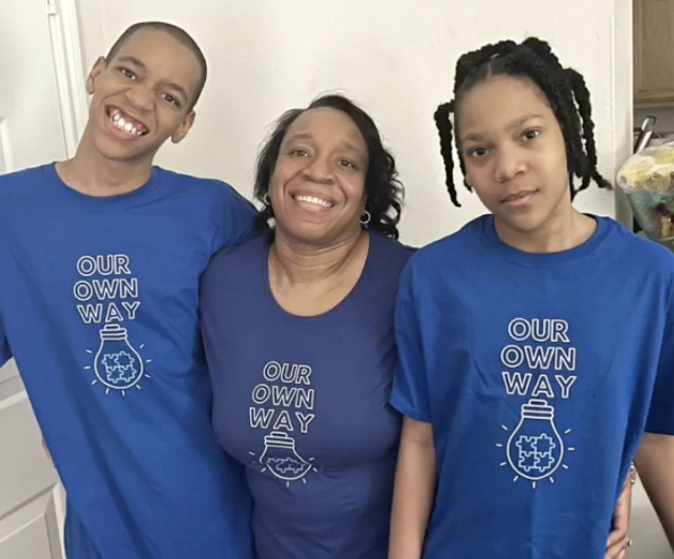 The store owner smiling with her two autistic sons, all wearing matching blue Our Own Way shirts.